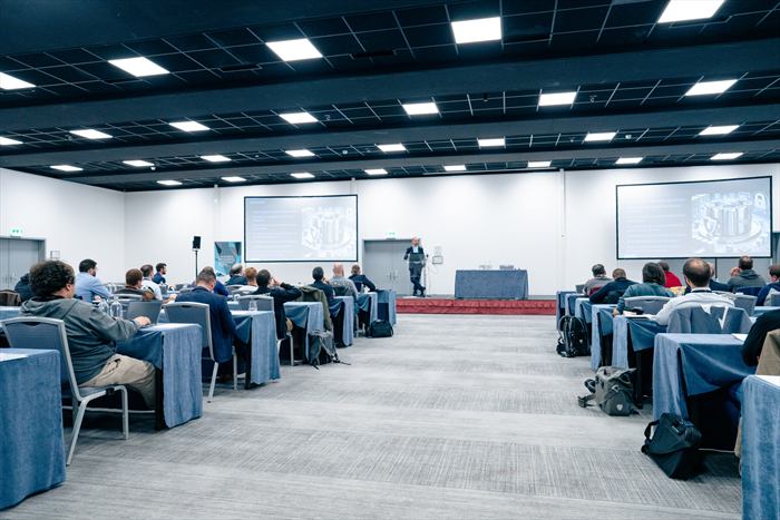 Vue d'ensemble de la salle plénière depuis le fond, avec le public de dos et l'intervenant sur l'estrade