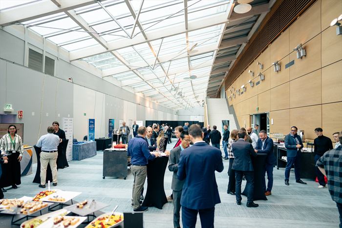 Participants échangeant debout dans l'espace de réception, buffet et stands des partenaires